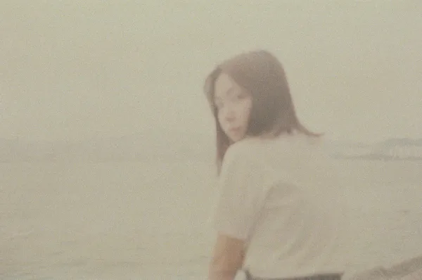Artistic blurred portrait of a woman at the beach with a calm sea backdrop.