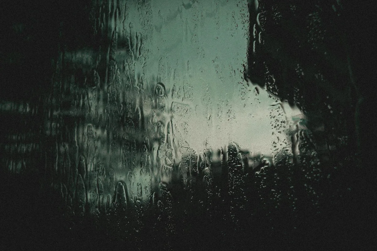 Gocce di pioggia artistiche sul vetro con atmosfera cupa. Ideale per sfondi.