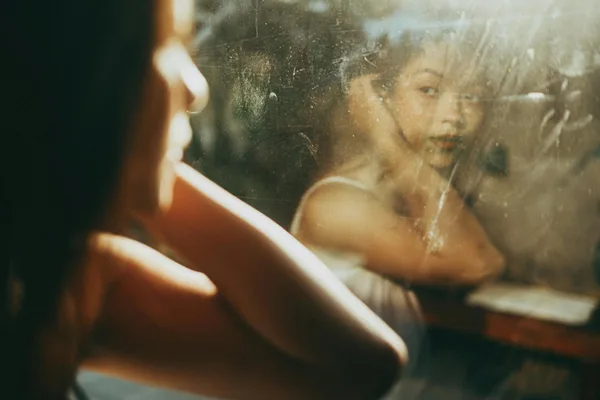 Artistic portrait capturing a woman's reflection in a window with warm sunlight.