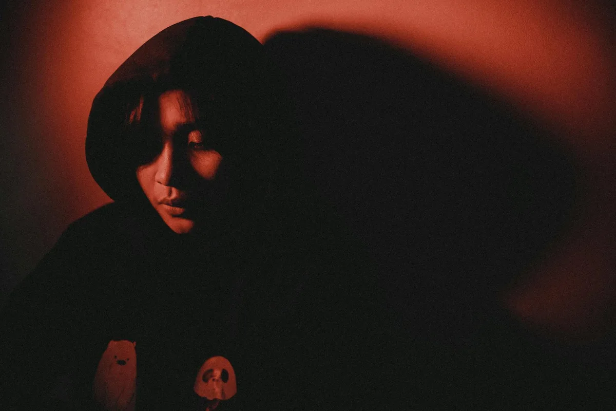 Persona incappucciata illuminata da luce rossa, ombre scure. Ideale per sfondi.