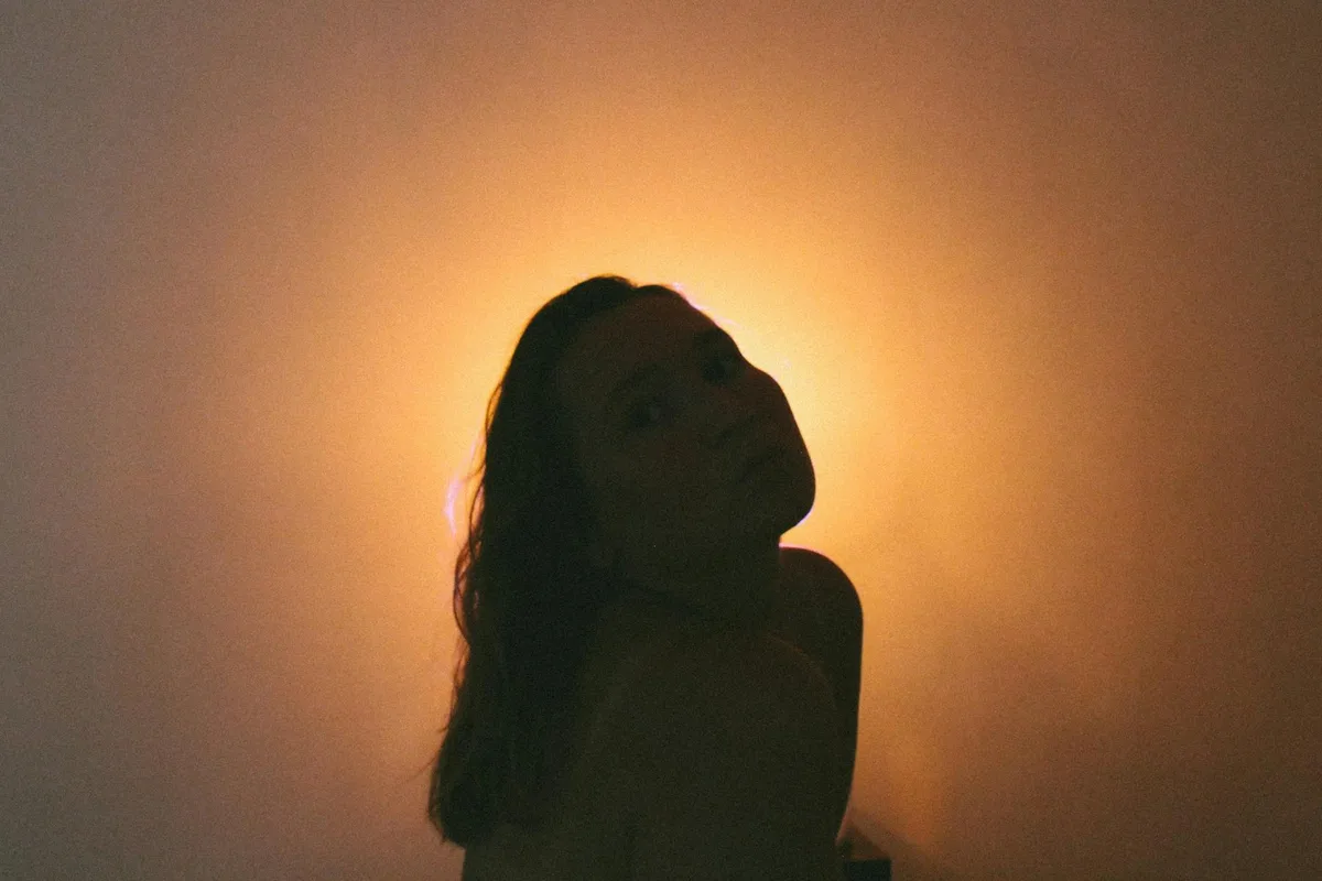 Silhouette femminile artistica controluce con luce gialla calda, atmosfera drammatica