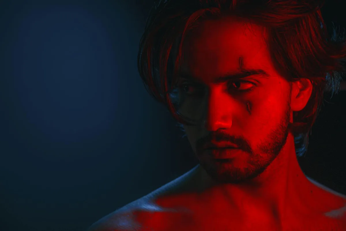 Primo piano uomo con luci rosse e blu, effetto drammatico.