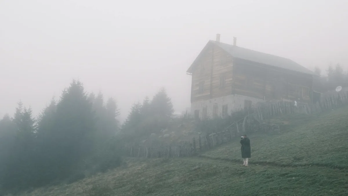 Neblige Hütte mit einsamer Figur auf dunstigem Hügel