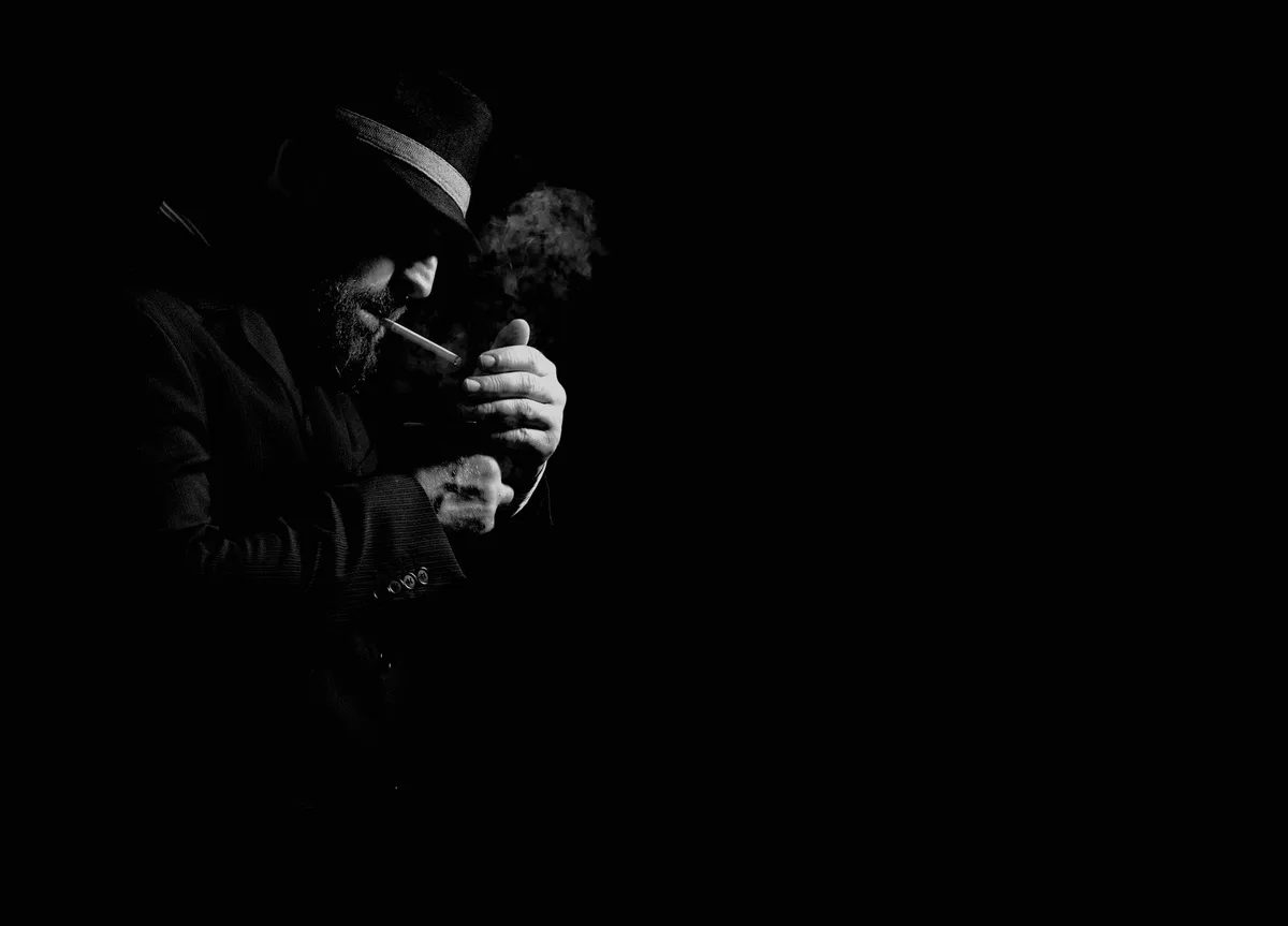 Ritratto drammatico b/n di uomo che accende sigaretta in penombra.