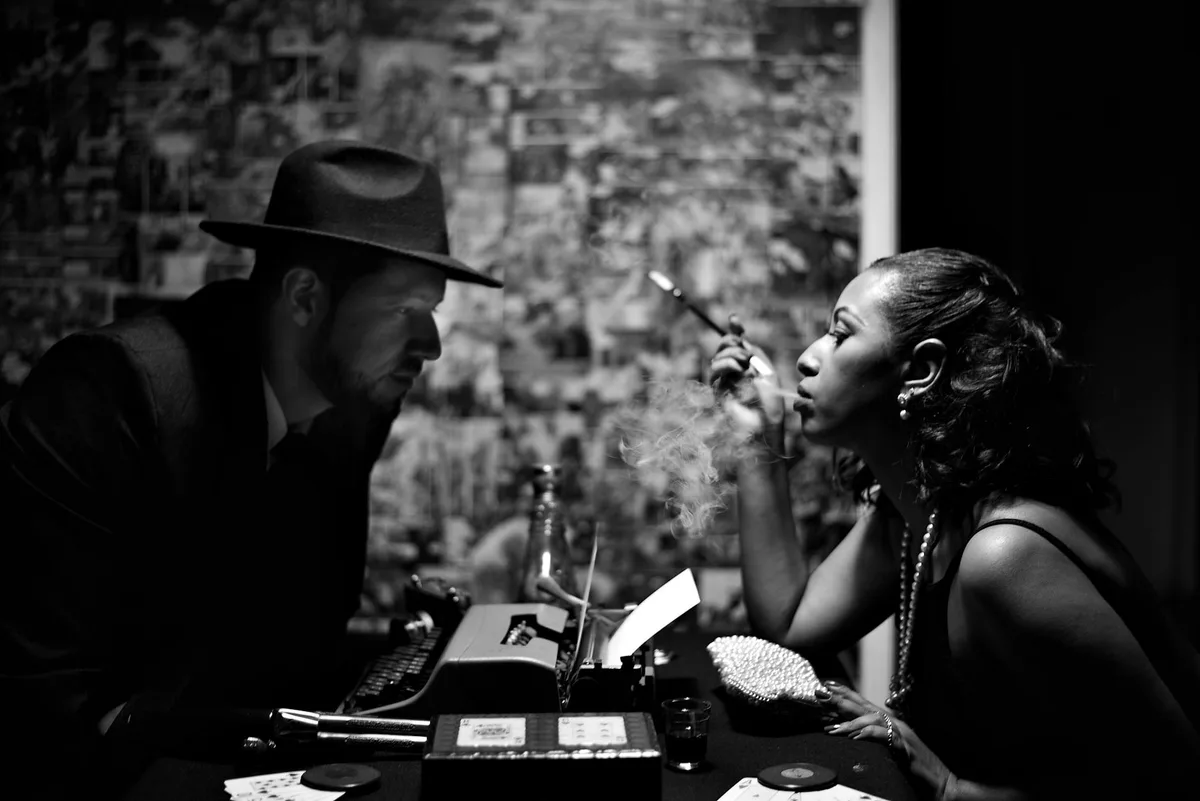 Scena vintage drammatica b/n con donna fuma e uomo con cappello.