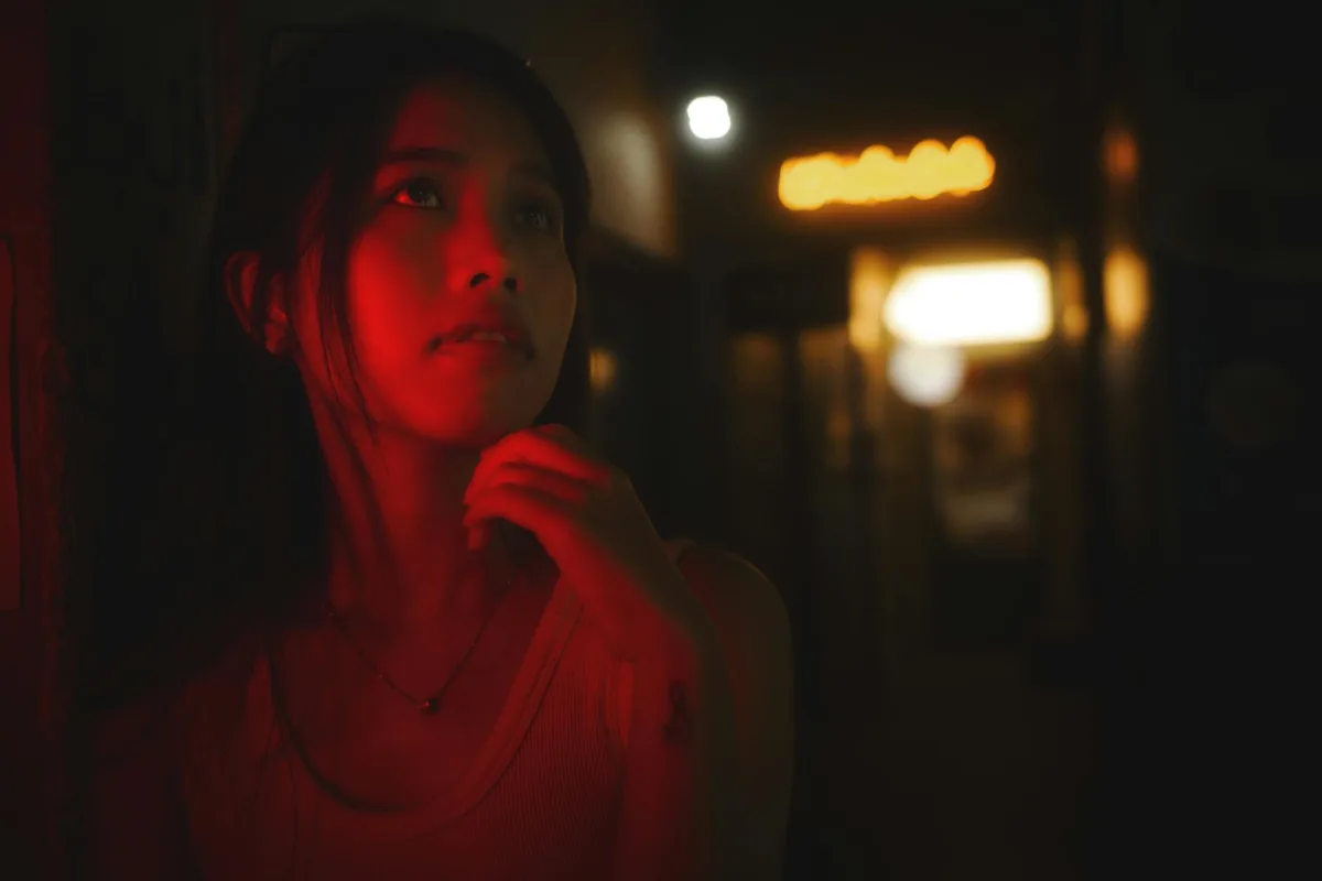 Mulher misteriosa em corredor vermelho à noite, clima contemplativo.