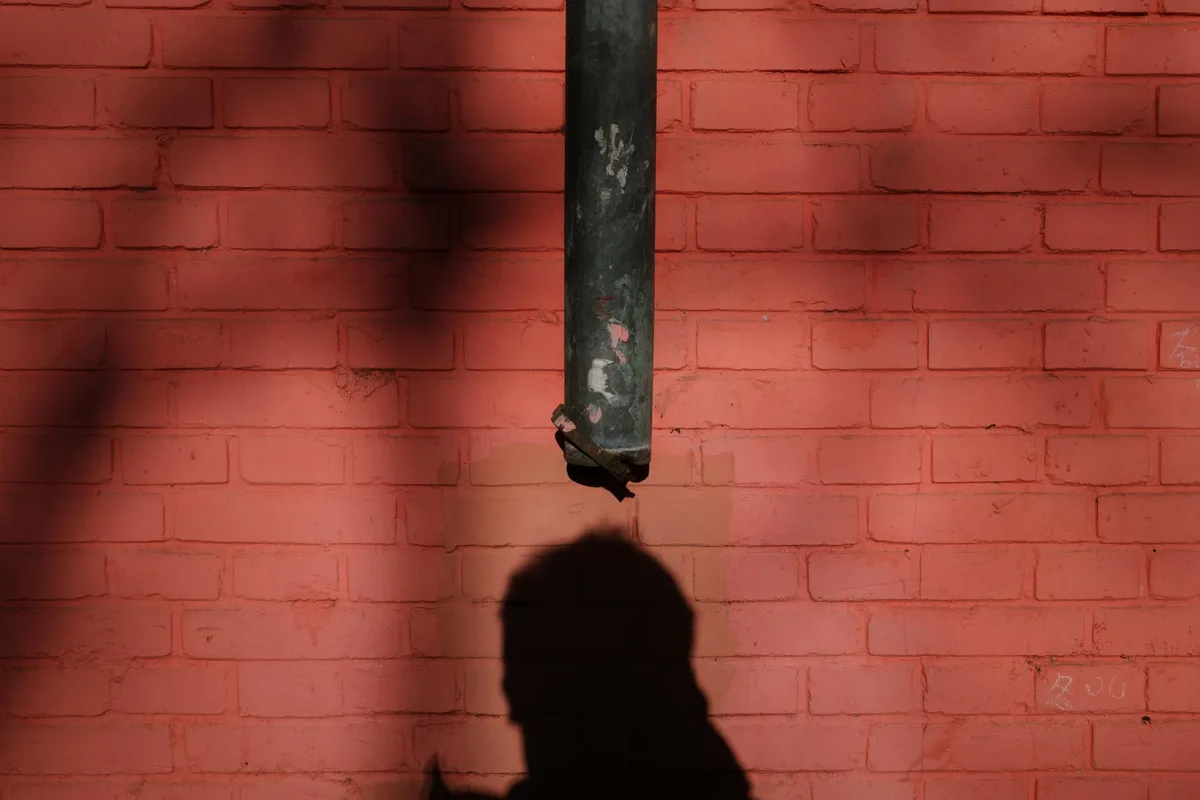 Ombra di una persona su muro di mattoni rossi con tubo, atmosfera urbana