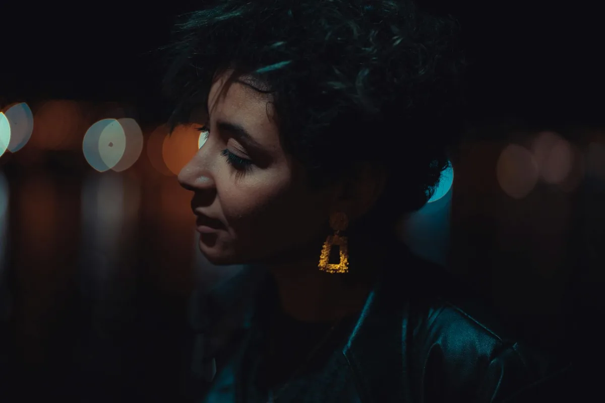 보케 조명 아래 밤에 포착된 숏컷과 귀걸이를 한 여성의 측면 프로필