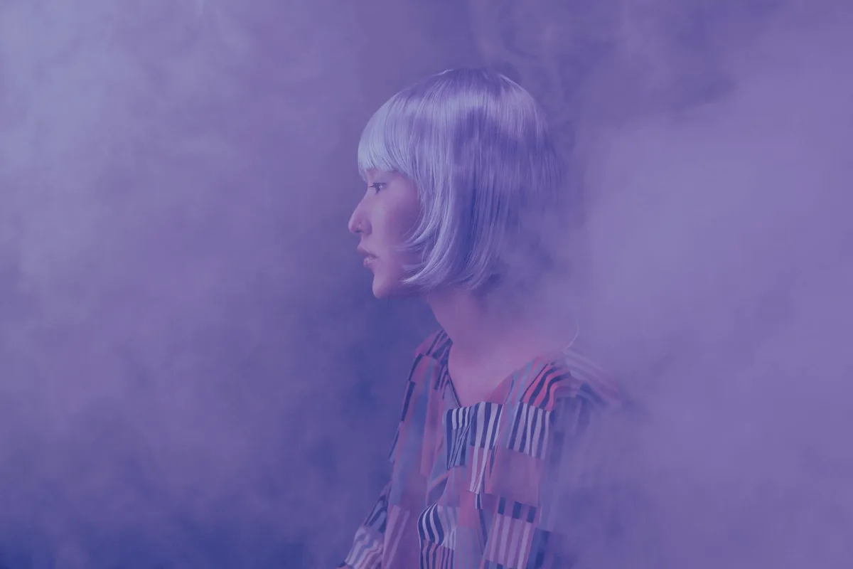 Side view of a fashionable woman in a smoky, conceptual studio setting.