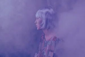 Side view of a fashionable woman in a smoky, conceptual studio setting.