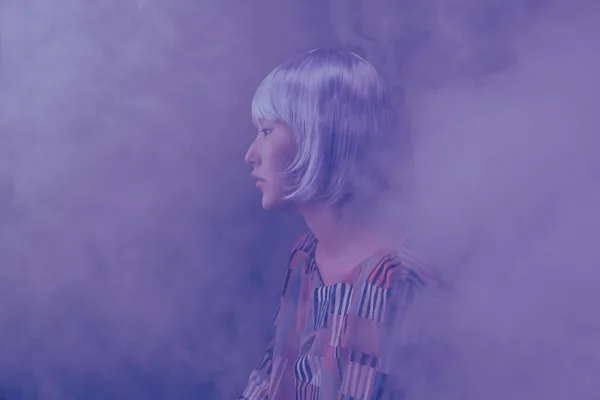 Side view of a fashionable woman in a smoky, conceptual studio setting.