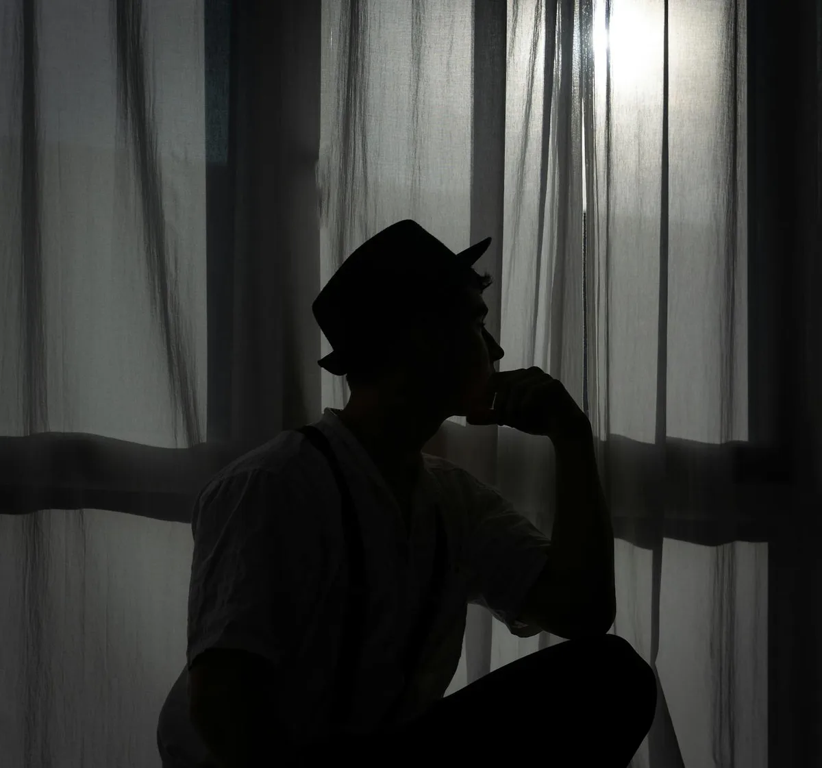 Silhouette di uomo con cappello seduto alla finestra, atmosfera malinconica