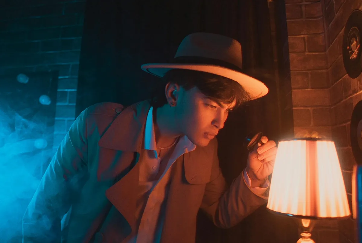 Homem estiloso de chapéu e trench coat investigando com lanterna e lupa