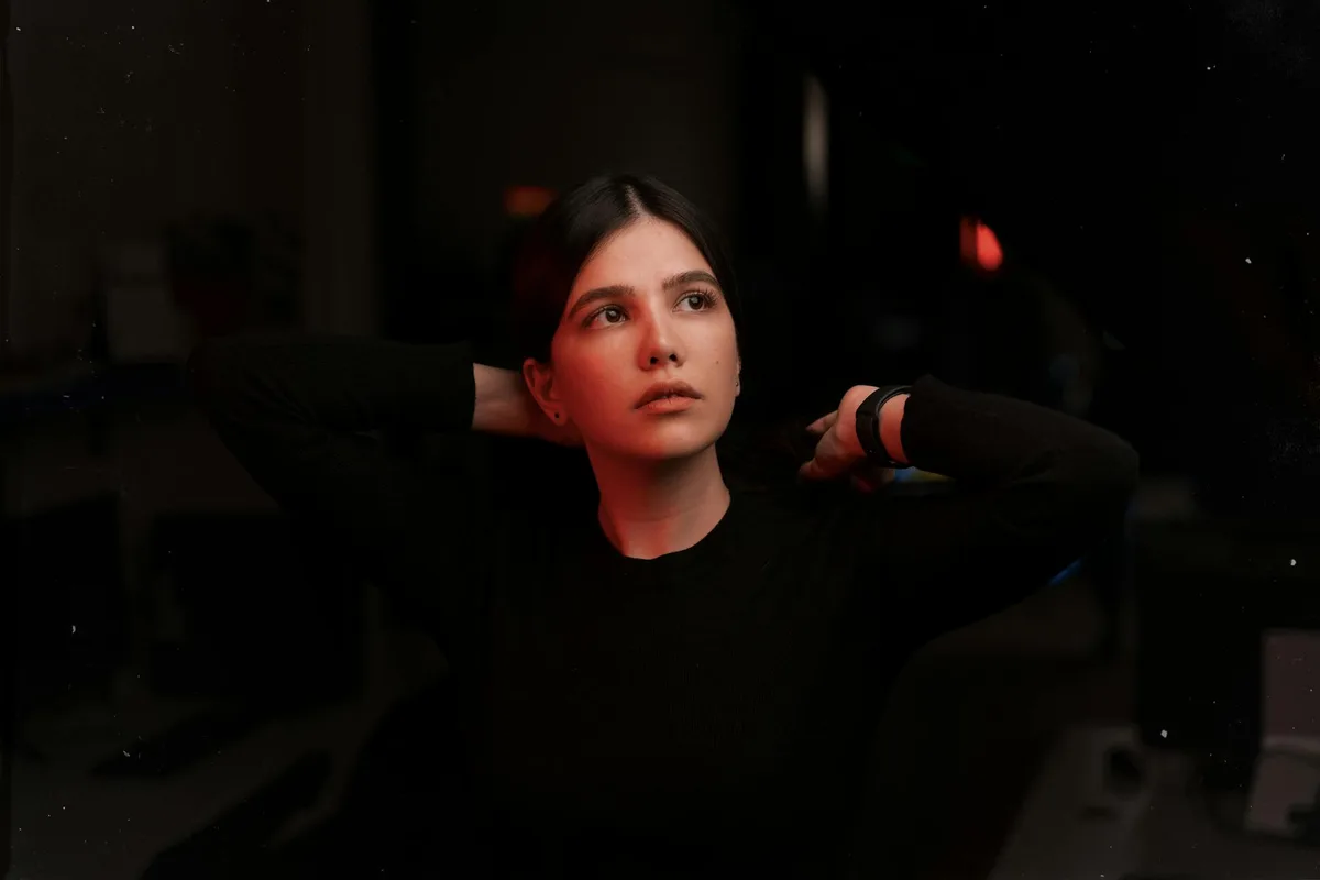 어두운 배경에서 검은 옷을 입고 머리를 정리하는 생각에 잠긴 여성