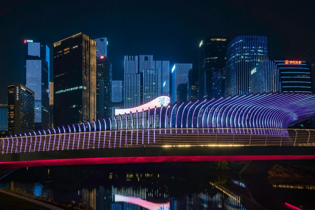 Paesaggio urbano vibrante con grattacieli illuminati e ponte futuristico al neon di notte