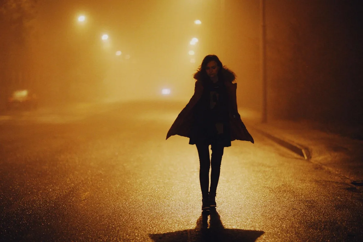 모피 코트 입은 여성이 안개 낀 밤거리를 걷는 드라마틱한 장면