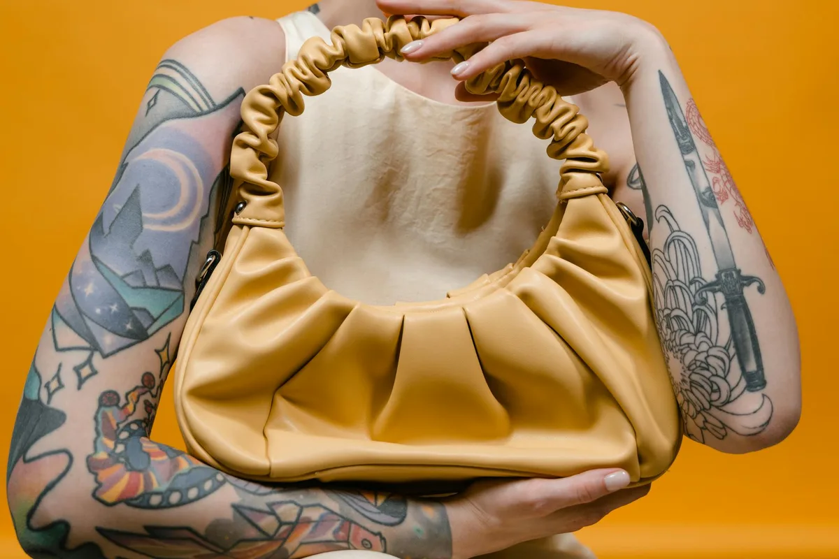 Tätowierter Arm mit eleganter gelber Lederhandtasche