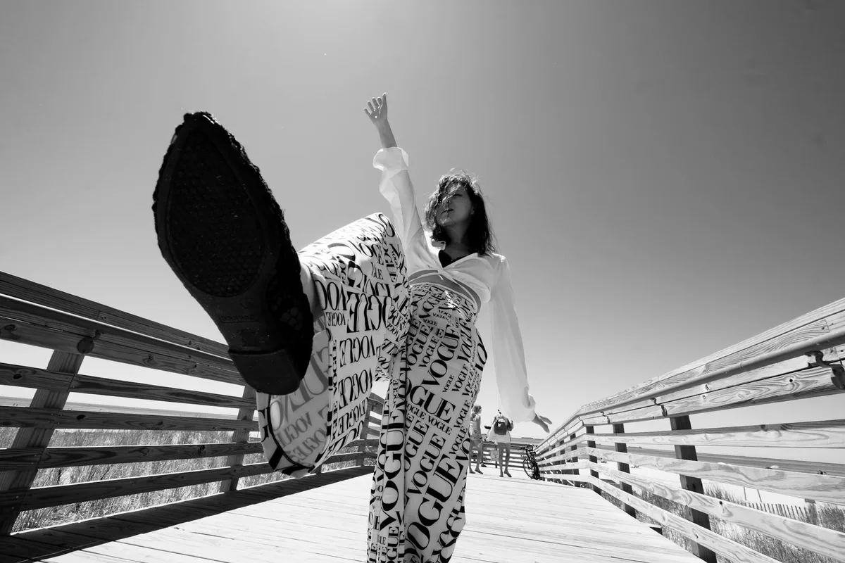 Modische Frau posiert auf Boardwalk mit Vogue-Print-Hose in dynamisch-monochromem Shot
