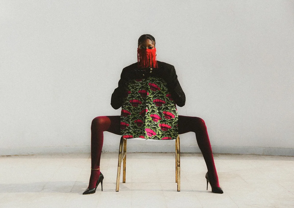 Pessoa com roupa estampada vibrante e acessórios vermelhos sentada em cadeira