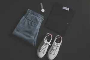 A stylish flat lay featuring jeans, t-shirt, sneakers, and a wristwatch on a dark background.