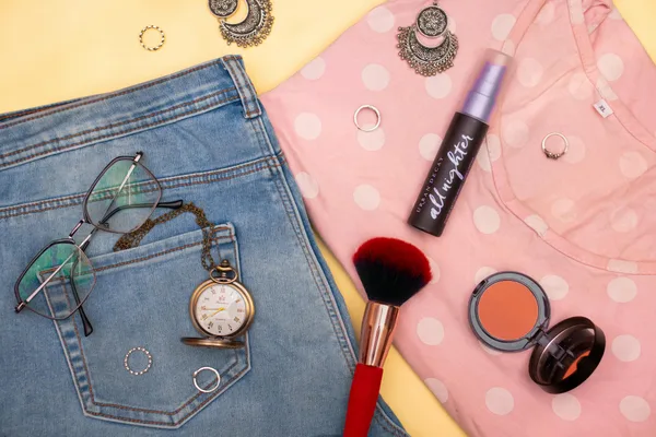 A stylish flat lay highlighting fashion essentials and makeup items on a polka-dot shirt.