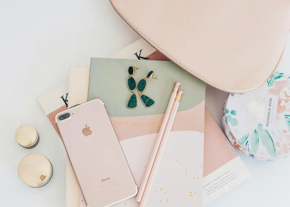 Flatlay stiloso con accessori oro rosa, iPhone e taccuino per tema moda femminile