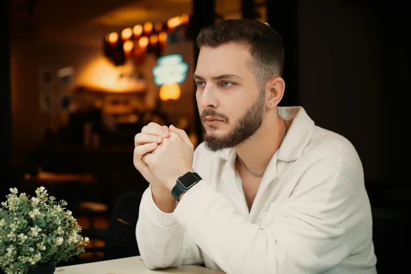 Uomo riflessivo al tavolino di un caffè, vibe moderno e stiloso