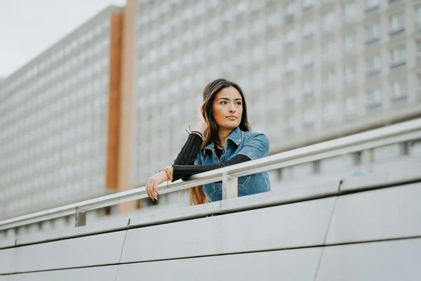 Frau in Jeansjacke an modernem Geländer in urbaner Umgebung