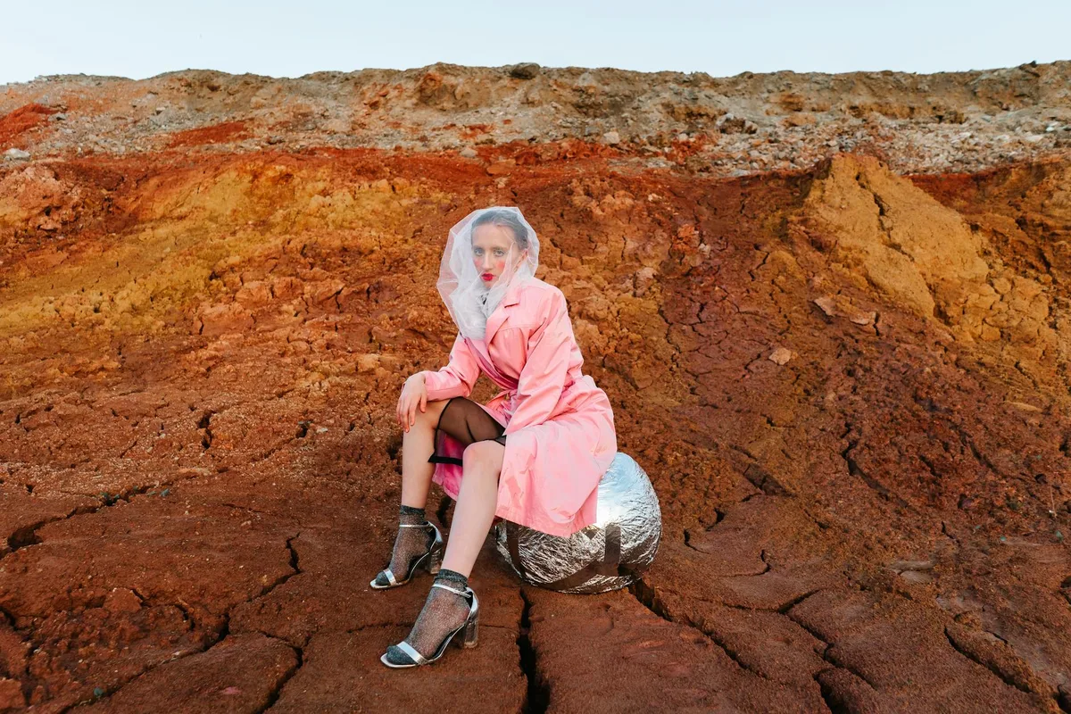 穿着未来主义时尚的女人在岩石地形上摆姿势，体现现代风格和创意。