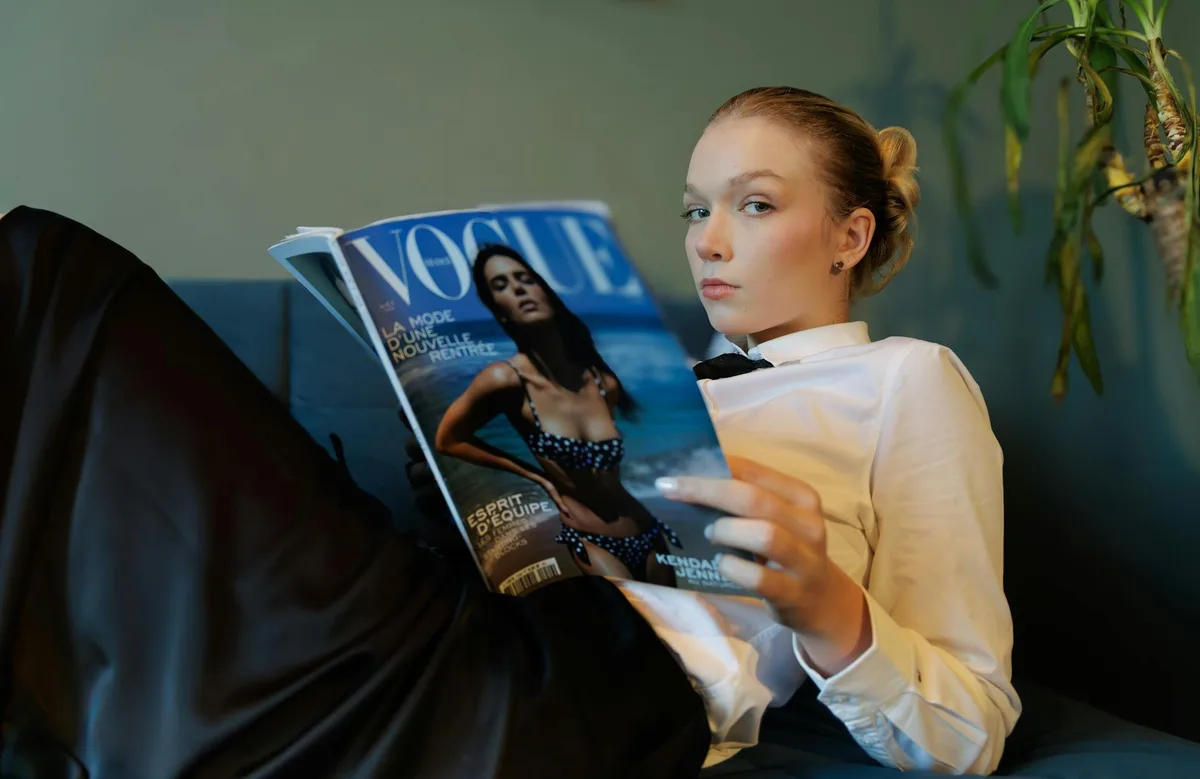 실내에서 정장 차림으로 보그를 읽는 젊은 여성의 스타일리시하고 편안한 모습
