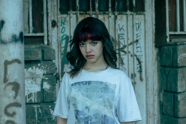 Junge Frau steht selbstbewusst vor einer Graffiti-Wand in urbaner Umgebung