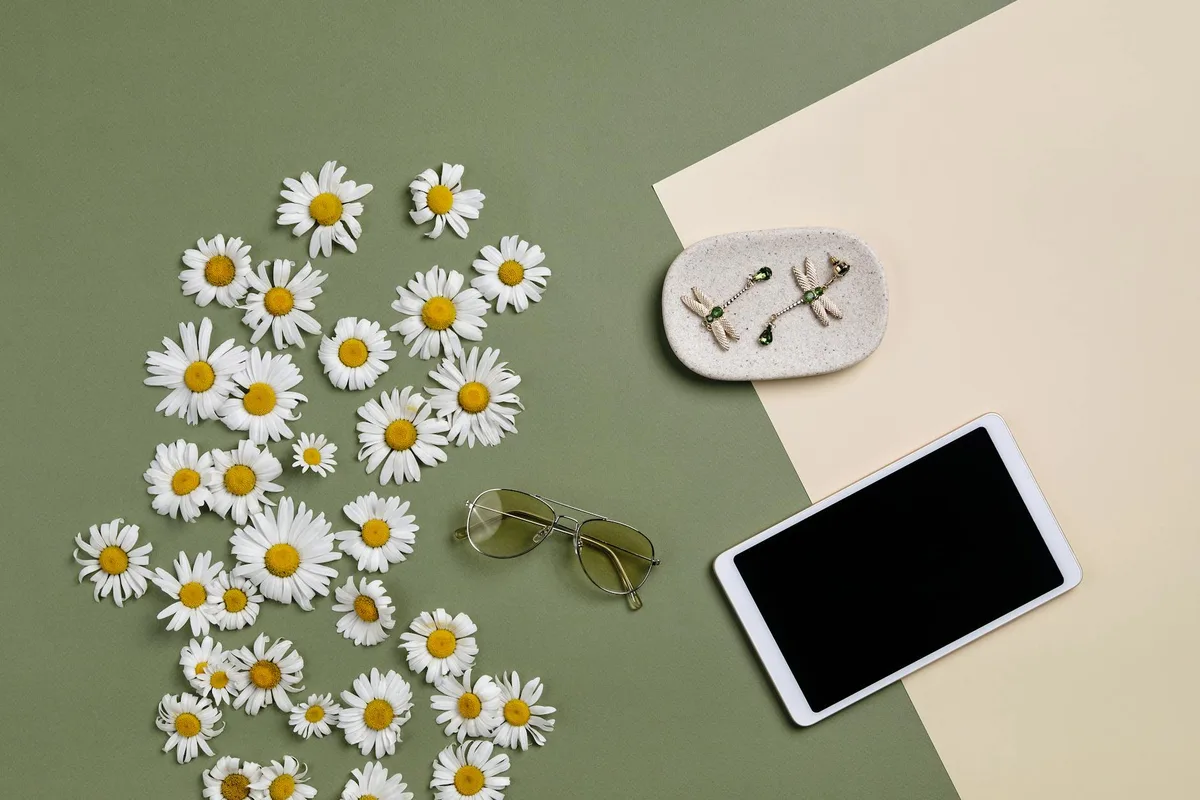 イエローデイジー、サングラス、タブレット、イヤリングをツートン背景に配置したシックなフラットレイ