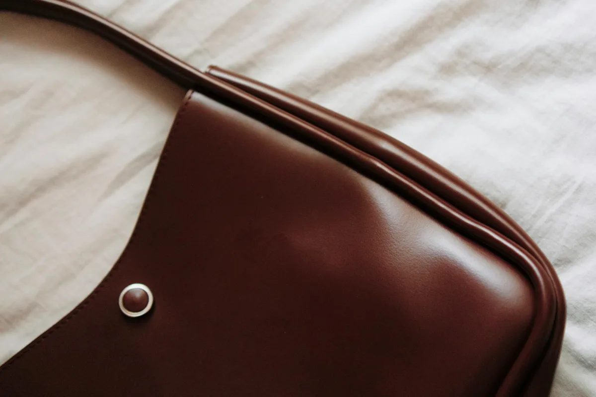 Close-up of a brown leather handbag laid on a light fabric surface, showcasing its elegant design.