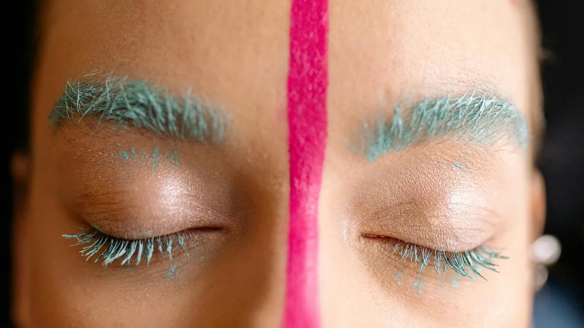 Close-up de maquiagem artística com sobrancelhas turquesa e listra rosa, estilos criativos.