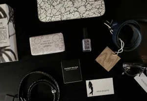 Elegant flatlay featuring accessories, a belt, nail polish, perfume, and eyeglasses on a dark background.
