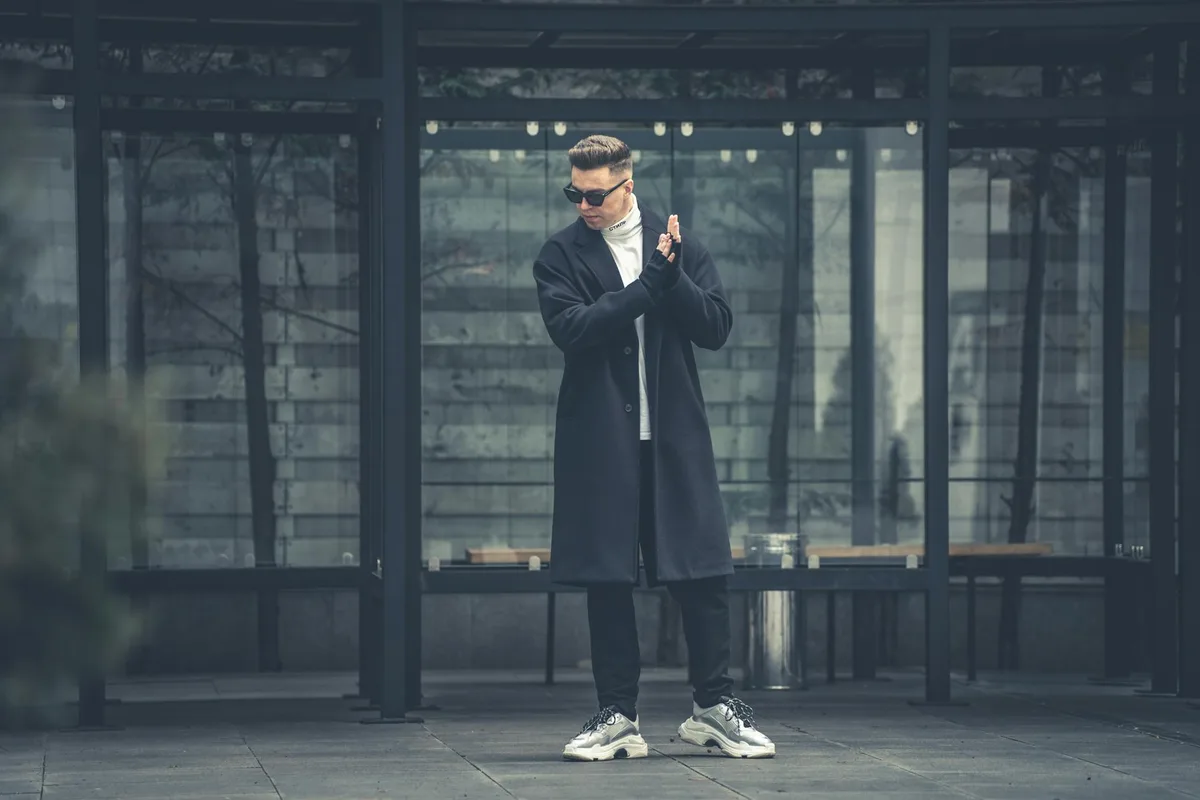 Modischer Mann mit langem Mantel und Sonnenbrille in moderner Urban-Umgebung