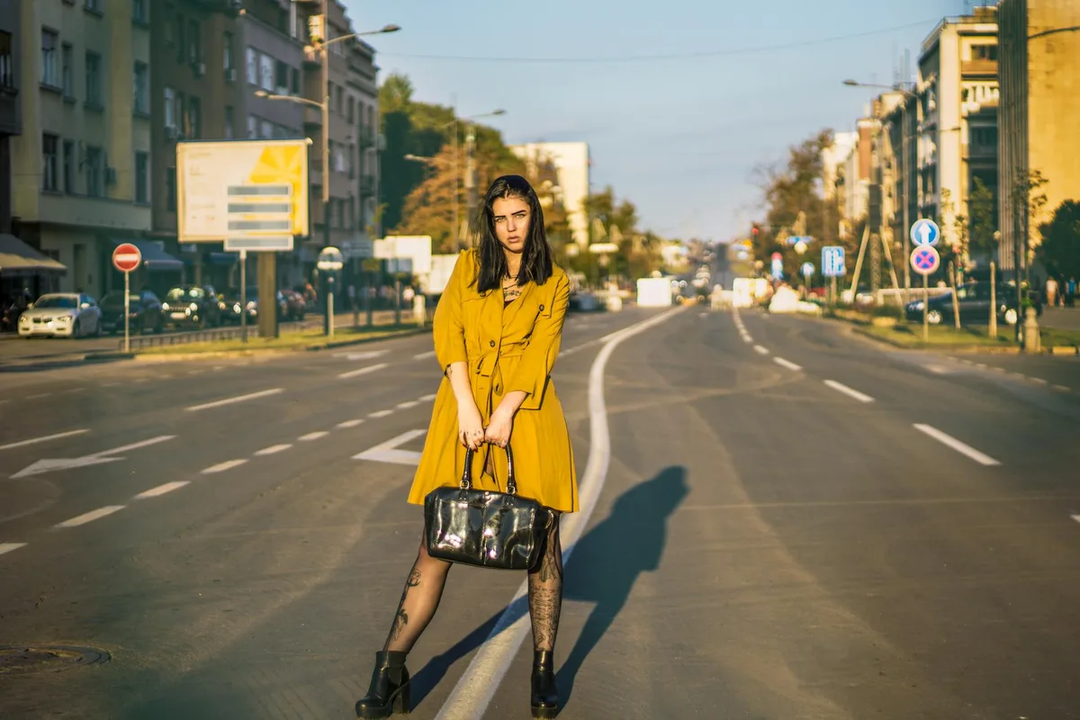 Femme élégante en manteau moutarde posant dans une rue vide