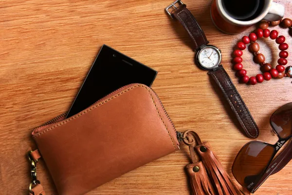 Flat lay of leather wallet, wristwatch, sunglasses, and coffee on wooden surface.