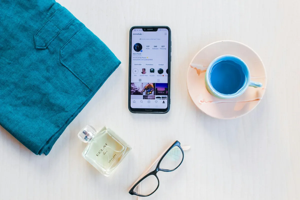 Вид сверху на современный смартфон с экраном, кружкой напитка и духами