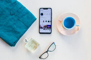 From above of modern cellphone with images on screen near mug of colorful drink and bottle of perfume