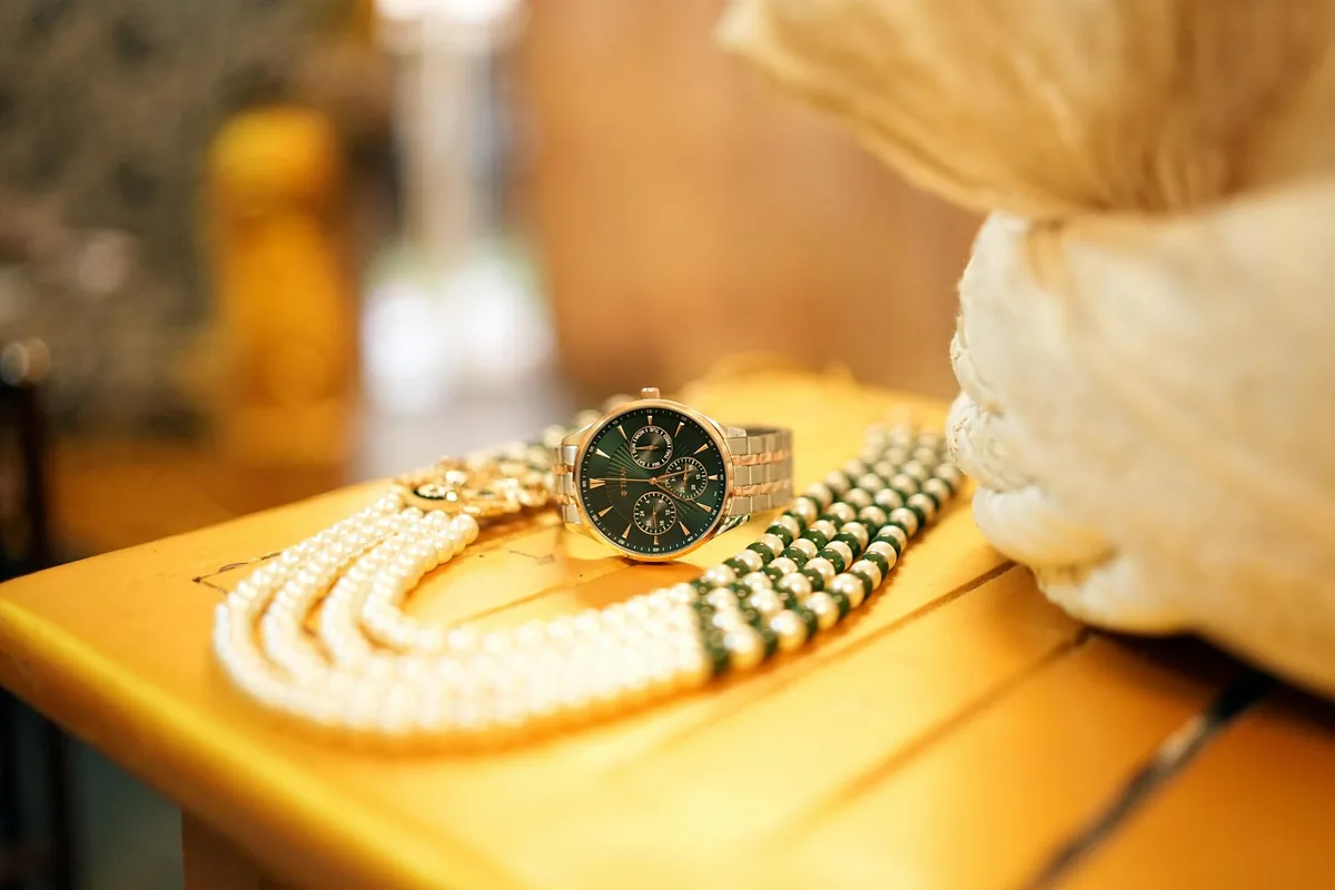 Montre en or et collier de perles sur table en bois, élégance et style.