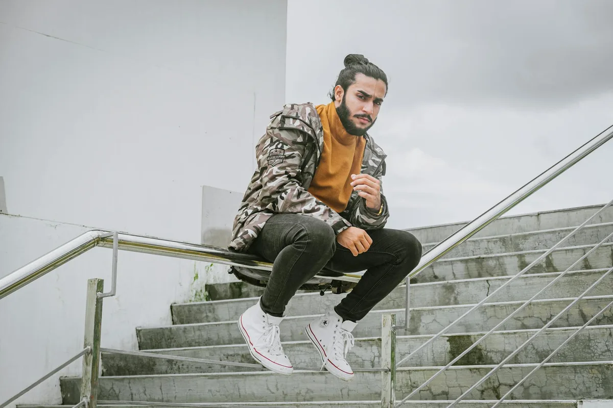 Homme en veste camouflage assis sur des rampes métalliques, style urbain.