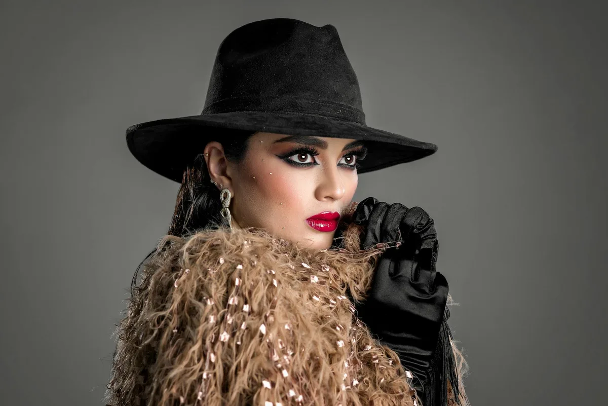 Женщина в черной шляпе с ярким макияжем и гламурным нарядом.