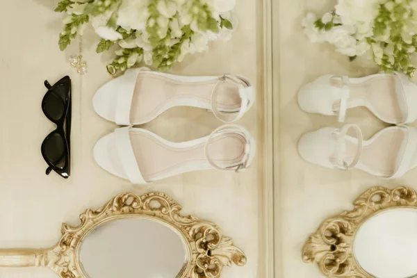 Stylish flat lay featuring white shoes, black sunglasses, and floral elements.