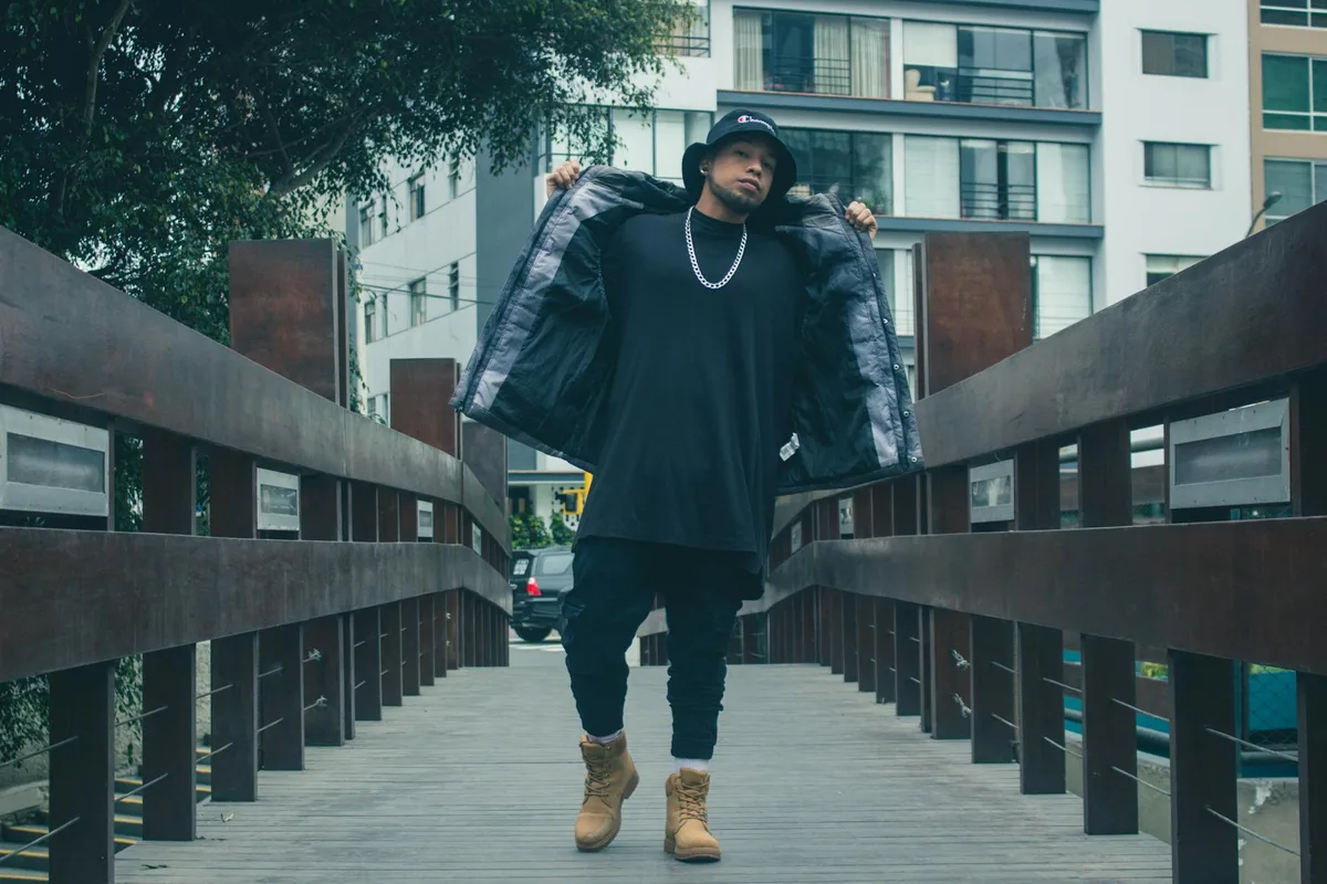 Uomo stiloso in streetwear urbano che posa con sicurezza su ponte cittadino