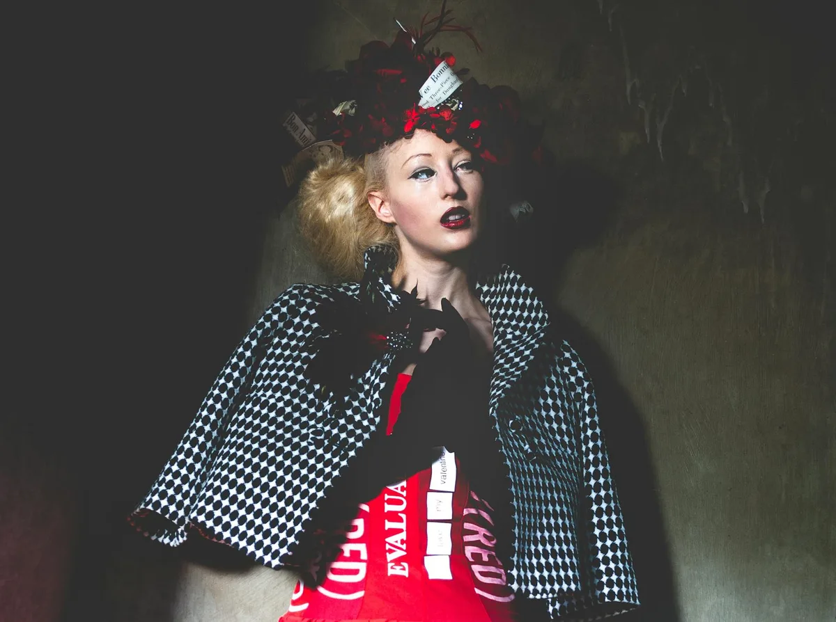 Nachdenkliche junge Frau mit blonden Haaren, hellem Make-up und Retro-Kostüm an schwarzer Wand