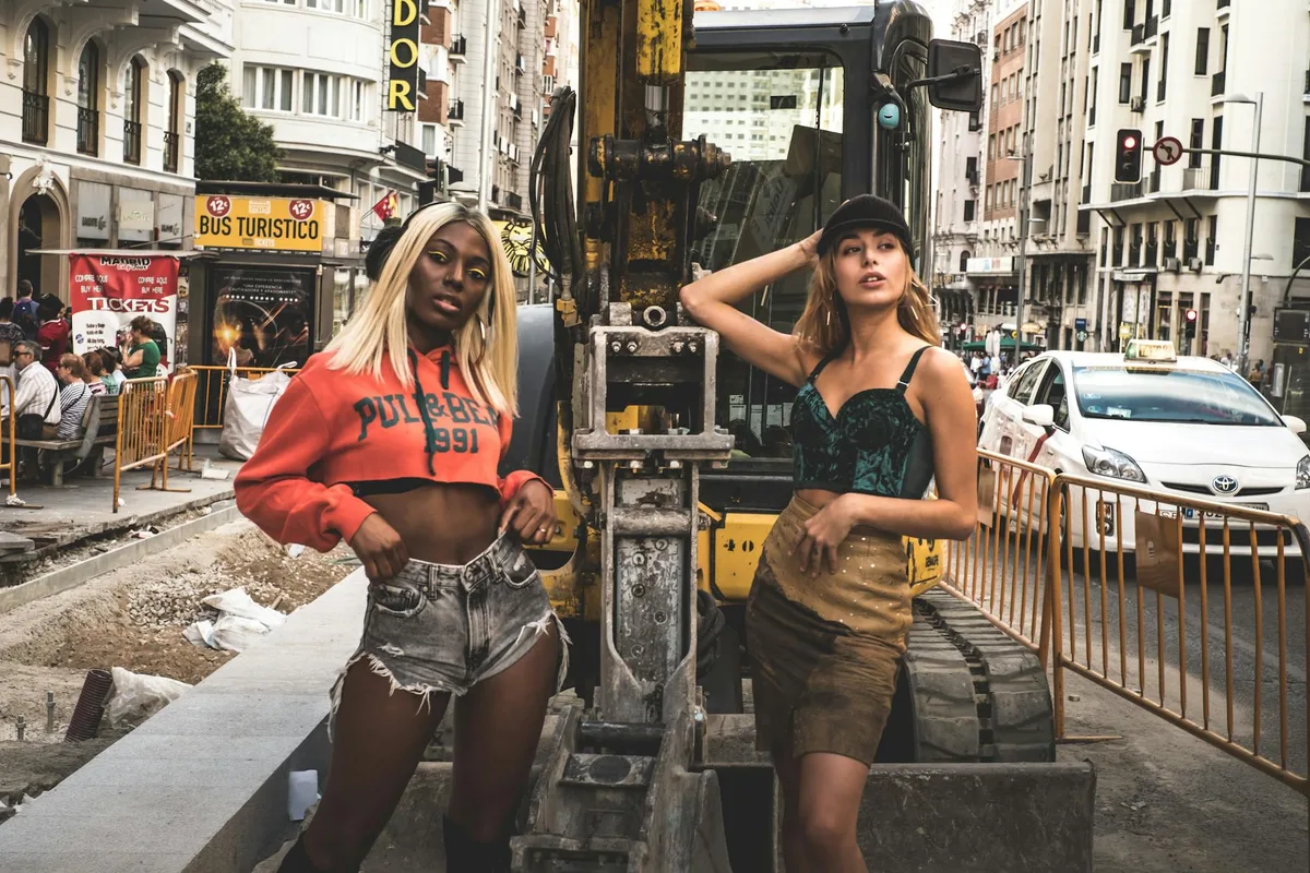 Two stylish women pose confidently at a street construction site in Madrid, Spain.
