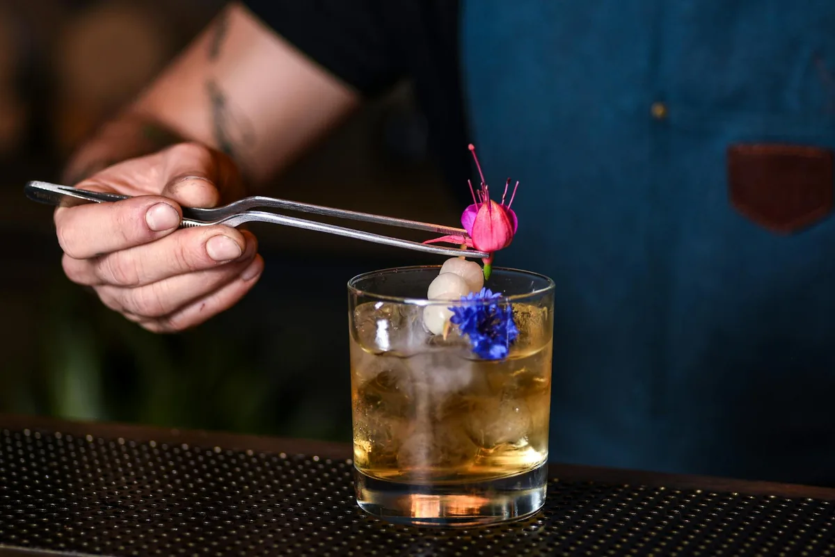 Barkeeper fügt Blütenschmuck zu einem Cocktail in einer New Yorker Bar hinzu.