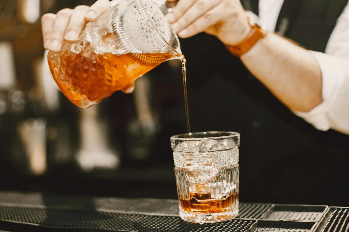 Barkeeper gießt fachmännisch einen Cocktail in ein Kristallglas und zeigt den Zubereitungsprozess.