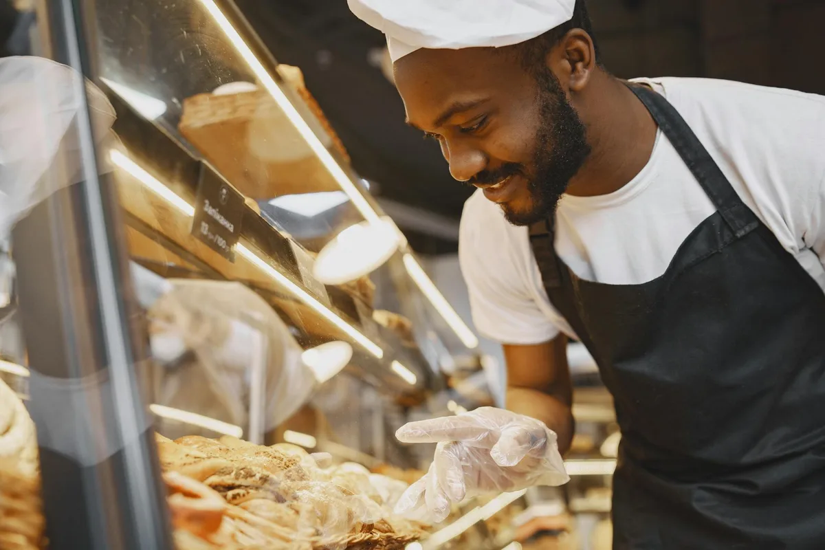 Boulanger souriant présentant des viennoiseries fraîches derrière une vitrine de boulangerie